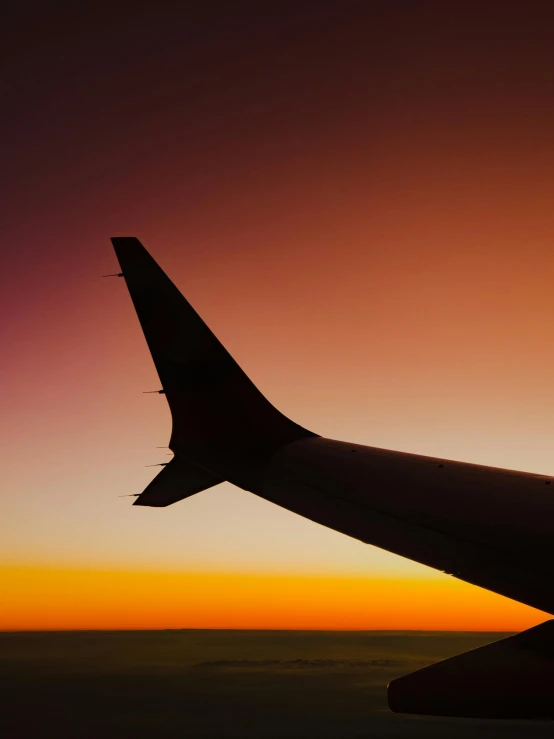 the wing of an airplane in silhouette at sunset