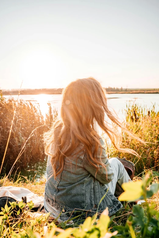 a woman sitting next to the water on a blanket