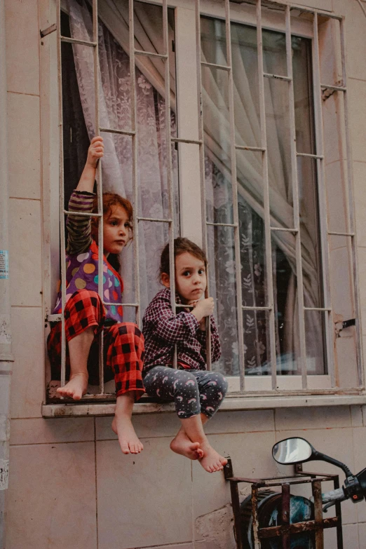 two children are sitting on a window ledge