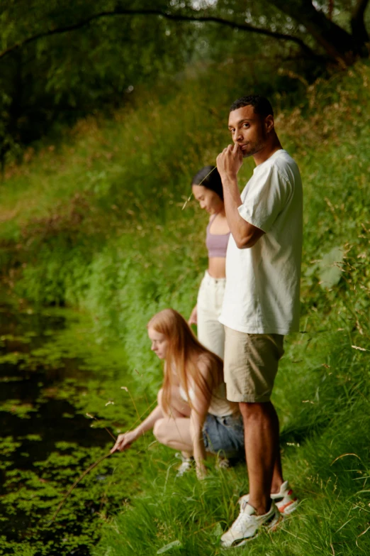 two women, one of them smoking a cigarette, are standing next to a body of water