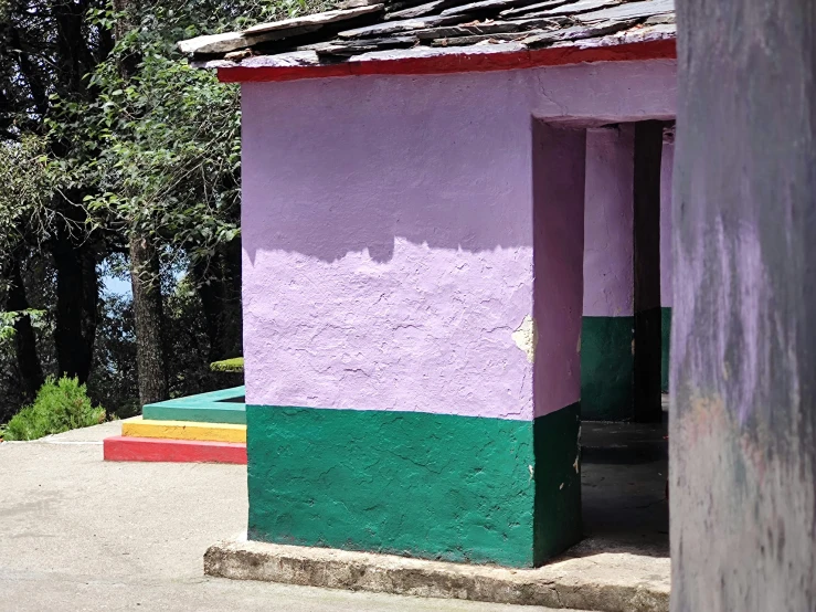 an out house with colored walls and a tree line behind it