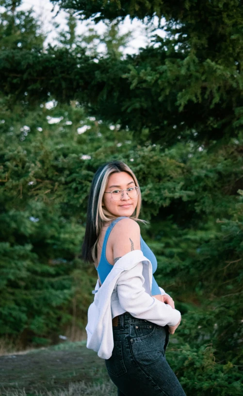 woman in front of trees wearing jeans and denim vest