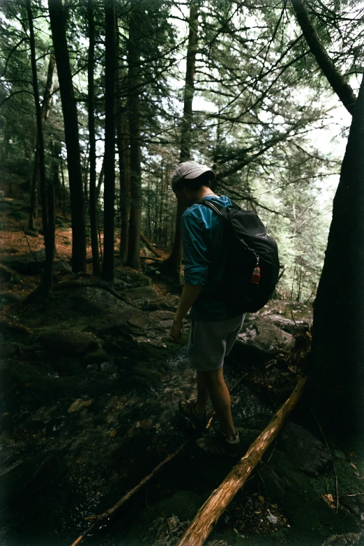 a man with a backpack stands on a log in the forest