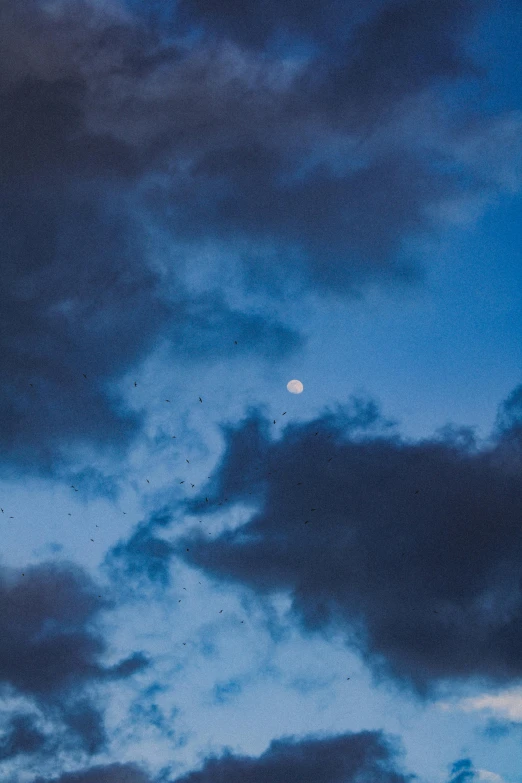 the dark sky is full of clouds and the moon in the distance