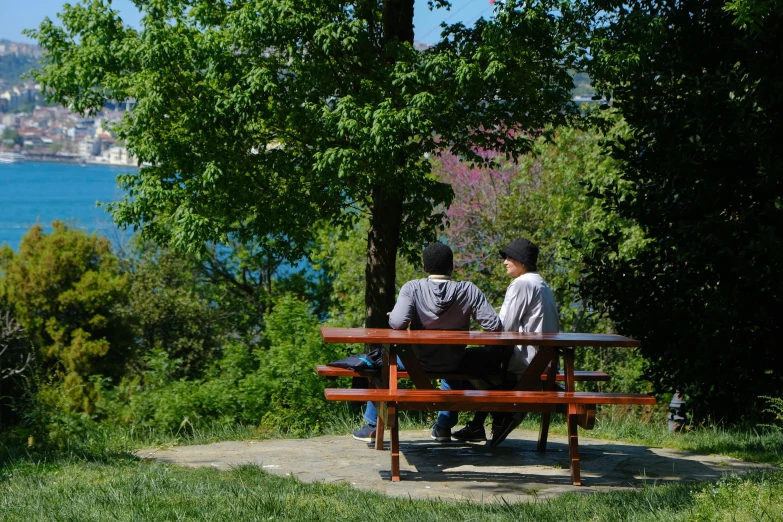 two men sitting on a park bench overlooking the water