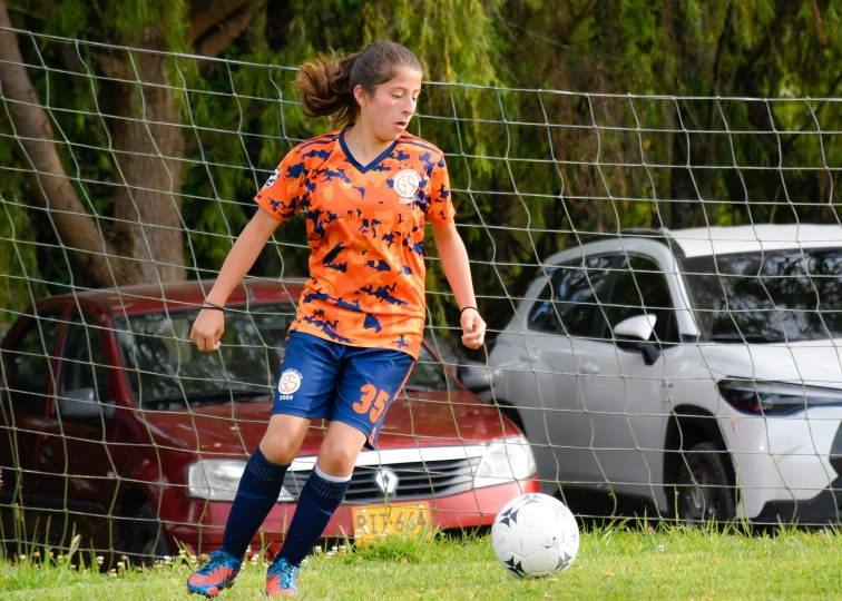 a girl with an orange jersey is kicking a soccer ball