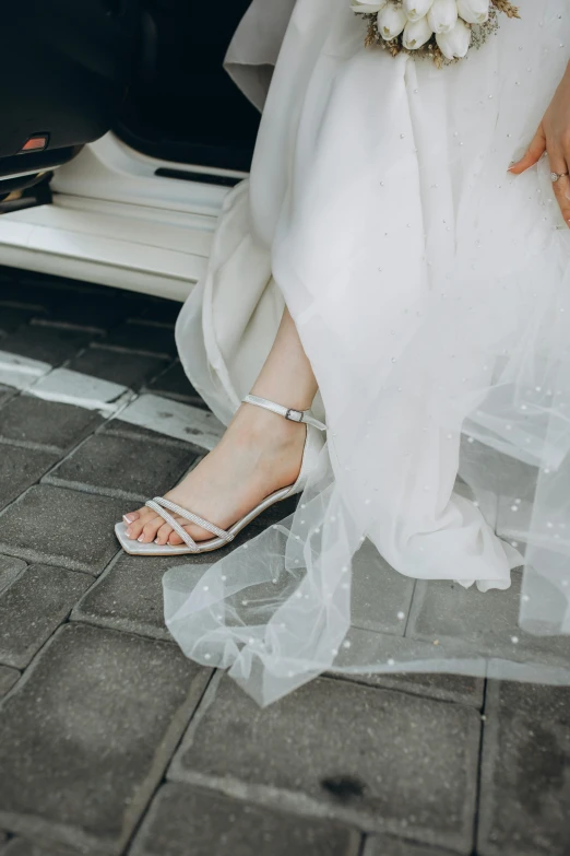a bride wearing bridal shoes in front of her wedding car