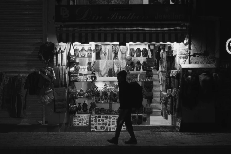 a dark street with storefronts and a man walking by