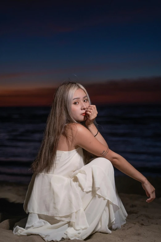 a woman in white sits on the beach at night