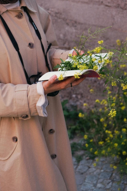 woman in trench coat holding flowers with hands