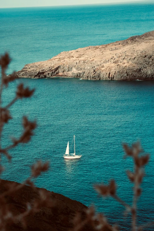 a white sailboat in the blue water near a rocky mountain