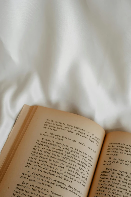 an open book is on a bed with a white linen