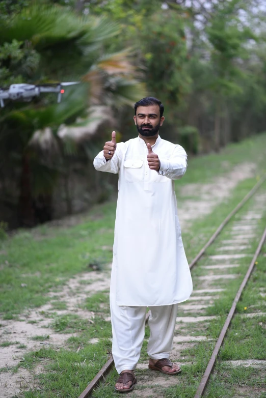 a man holding his thumbs up while posing in front of some train tracks