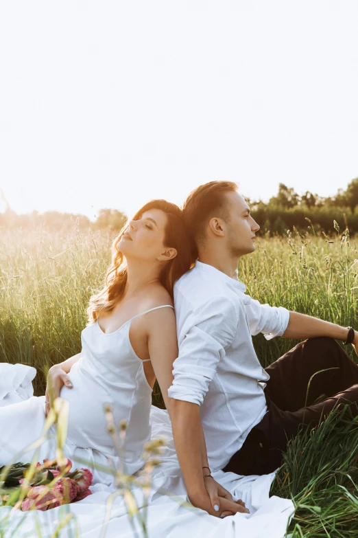 two people sitting in the grass with one person laying in the grass