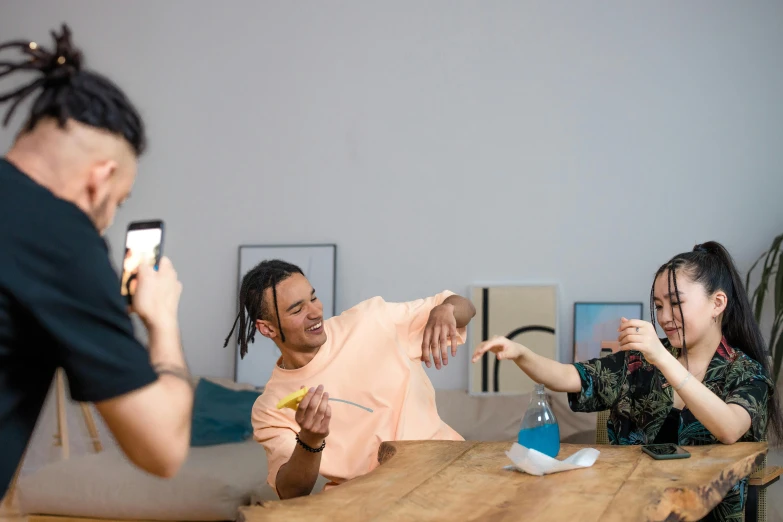 three people are sitting at a table and taking pos with cell phones