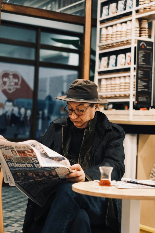 a man in glasses sitting at a table reading a newspaper