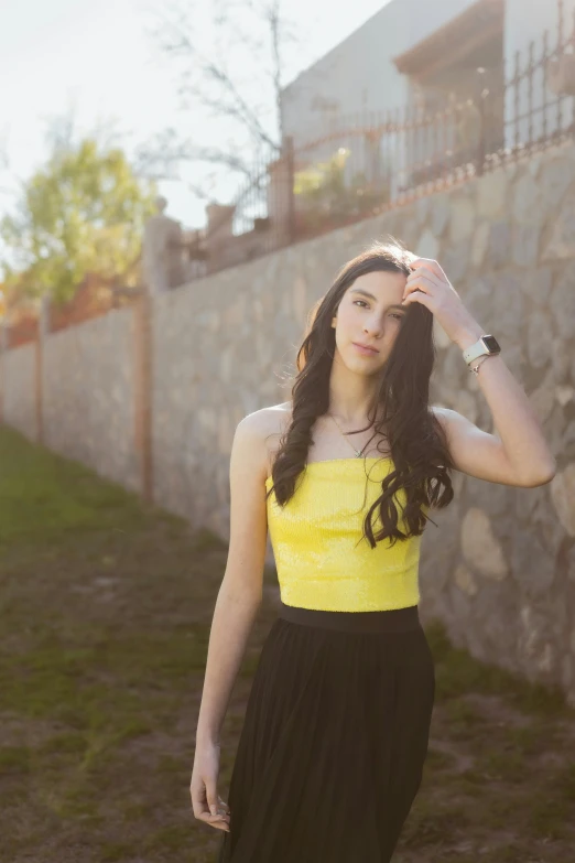 a woman in yellow top and black skirt by a stone wall