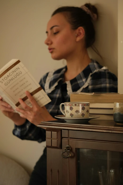 a woman reading a book and looking at a cup