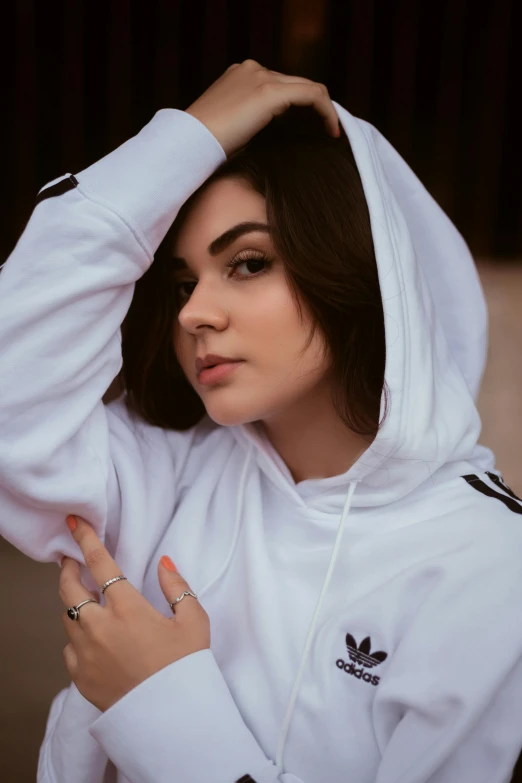 a girl with dark hair wears a white jacket and holds her hands near her head