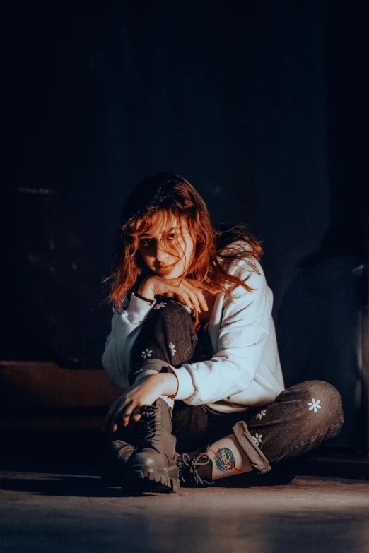 a red - haired woman sitting on the floor at night with her face against her chin and arms