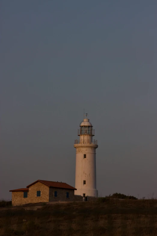 a lighthouse sits on top of a hill in the evening
