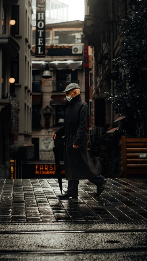 a man in winter clothes walking down a rain covered sidewalk