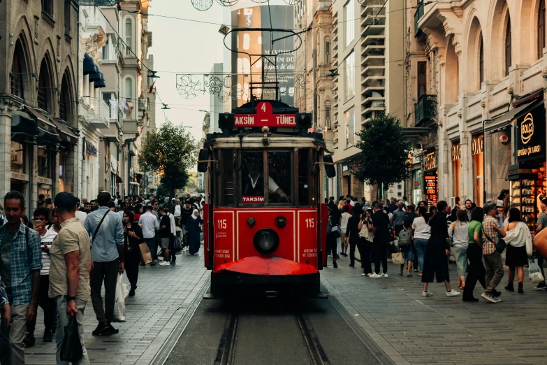 a crowd is walking on the street beside a red trolley