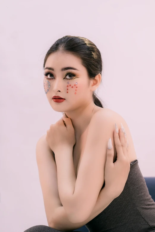 an asian woman with black makeup and a brown dress sits in the studio