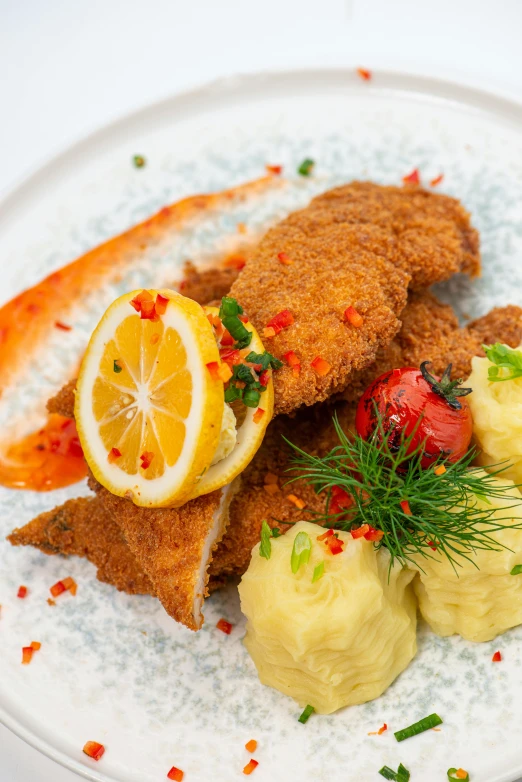 an oval white plate with breaded fried fish, mashed potatoes, and lemon slices