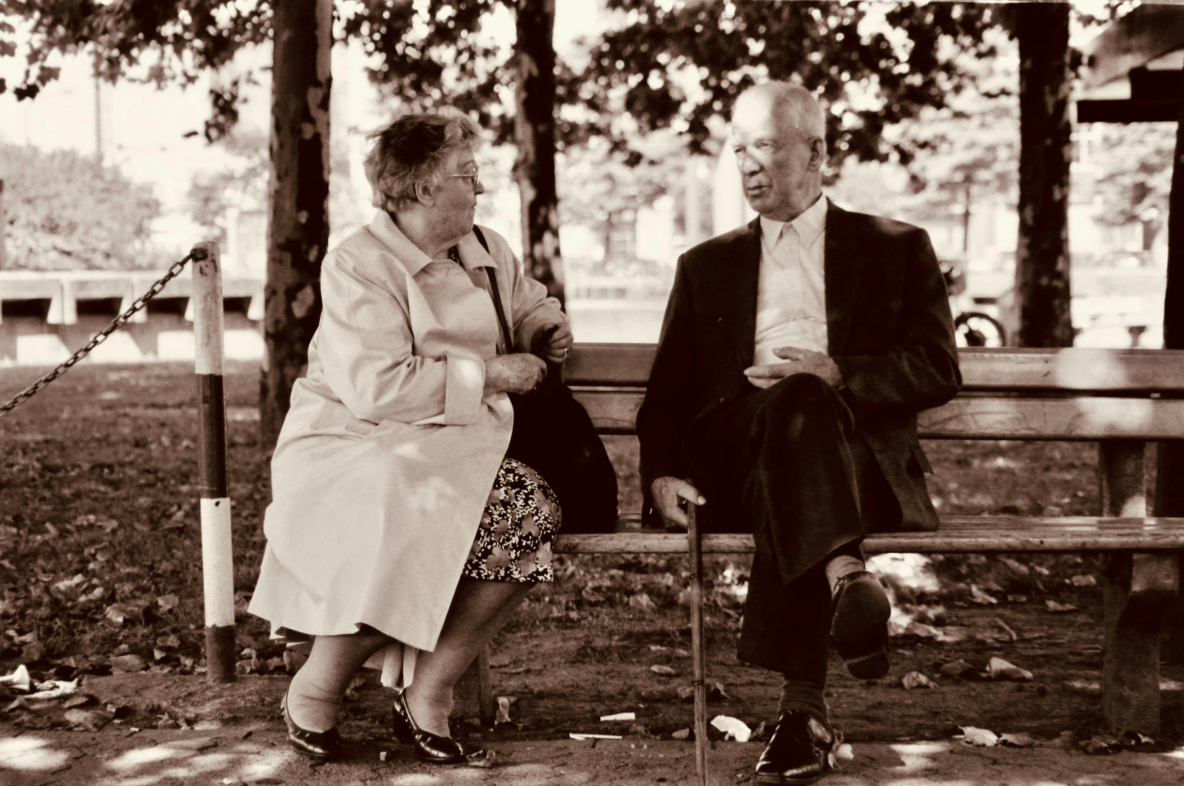 an old man sitting on a bench talking to a older lady