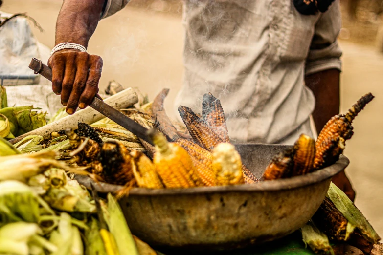 an african man cooking corn on the cob