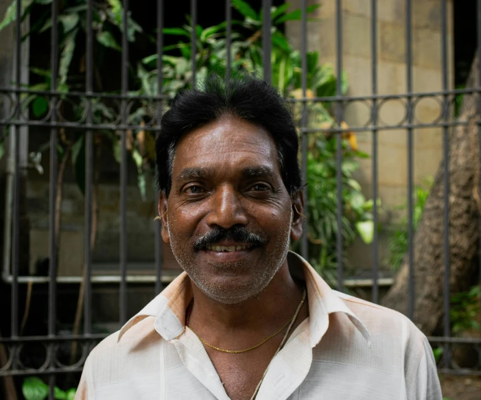 a man with a mustache stands in front of a fence