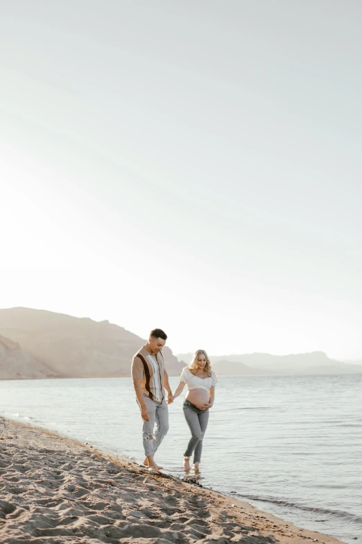 a pregnant woman and man standing next to each other at the beach