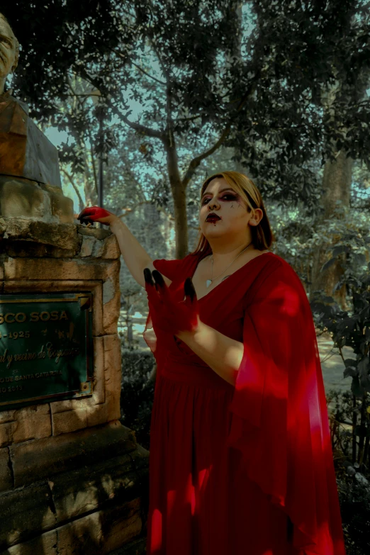 a woman wearing a red dress holding onto the back of a statue