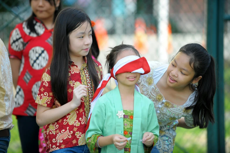 two girls wearing blind folded red hats and one girl is touching another girl's face