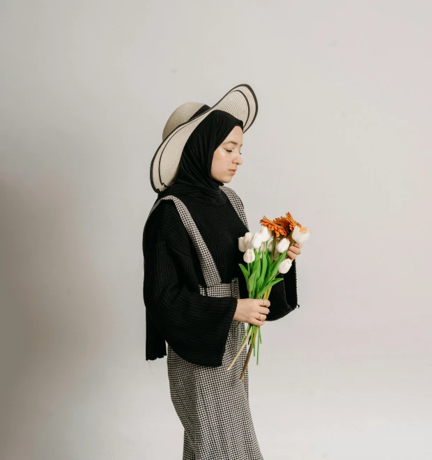 a woman in a dress holds flowers while wearing a large hat