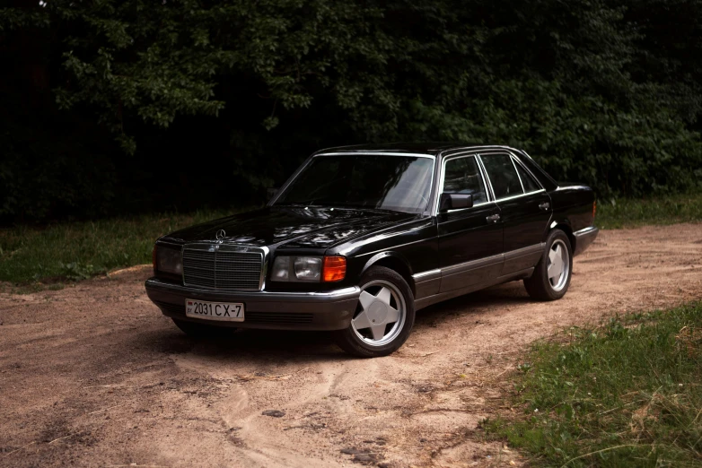 a black mercedes benz sits parked in the dirt