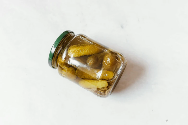 a mason jar filled with yellow pickles on top of a white surface