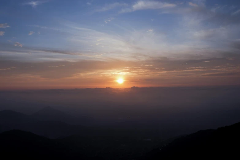 the sun rising over a mountain range with some clouds