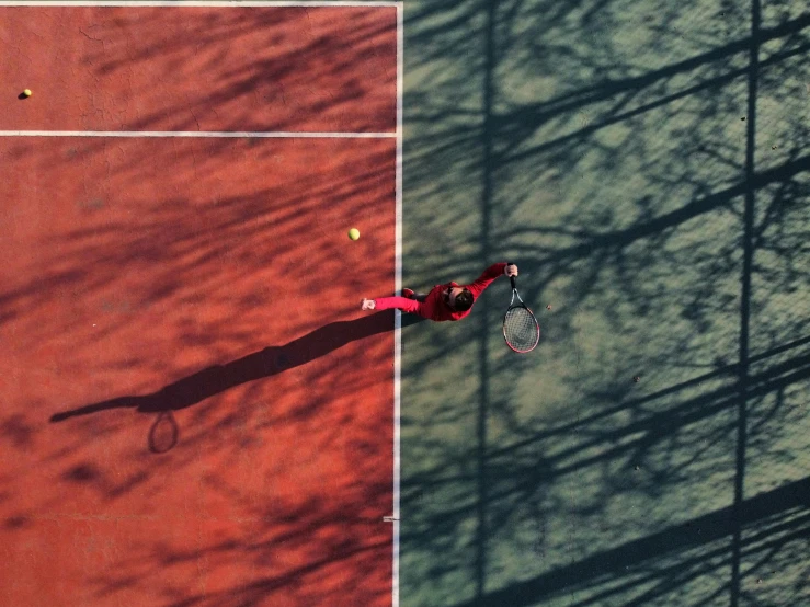 an overhead s of a man playing tennis on a red court