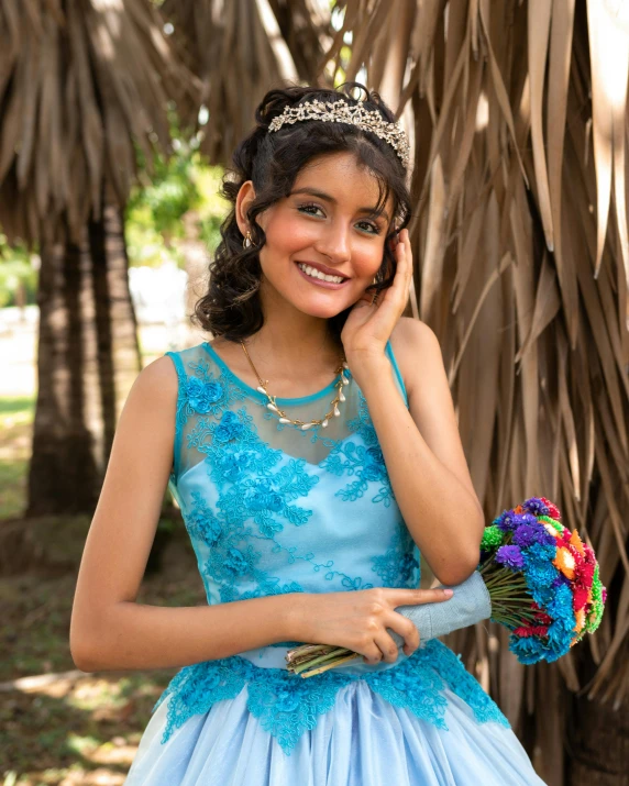 a young lady in a blue dress wearing a tiara and flowers holding a bridal bouquet