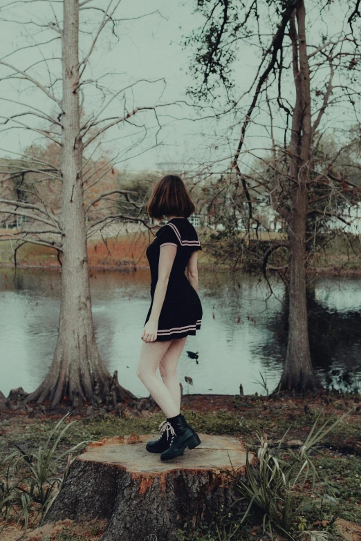 a girl in black dress standing on log next to water