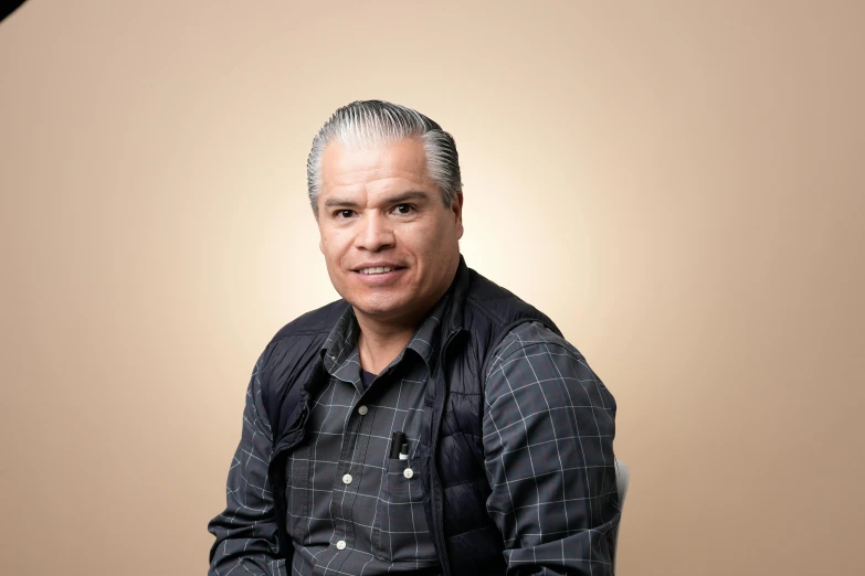 an older man poses for a pograph with a tan background