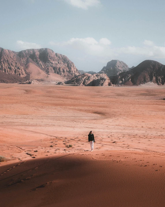 a lone woman walks through a red desert in the mountains