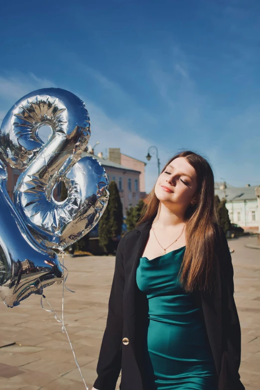 a woman in a green dress holding a shiny silver number twenty eight balloon