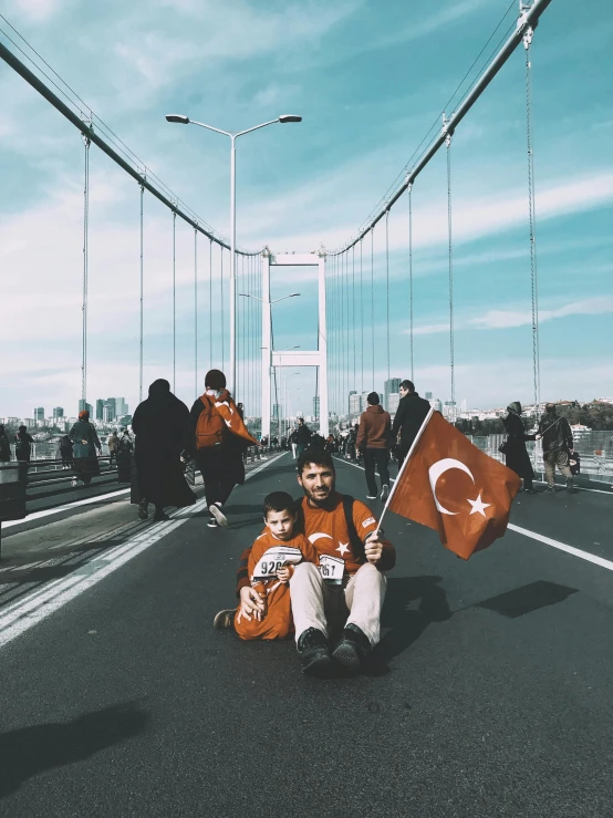 two people sitting on a bridge with an orange turkey flag