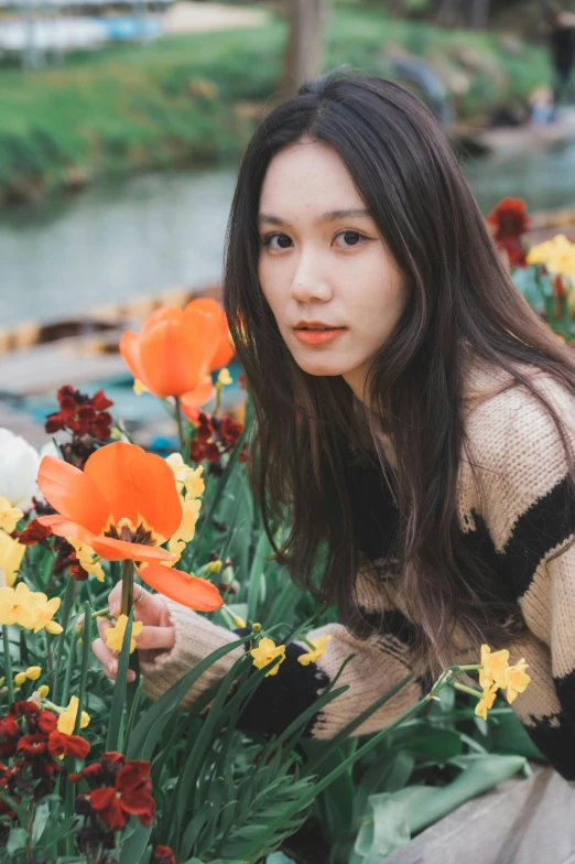 an asian woman leans over some flowers