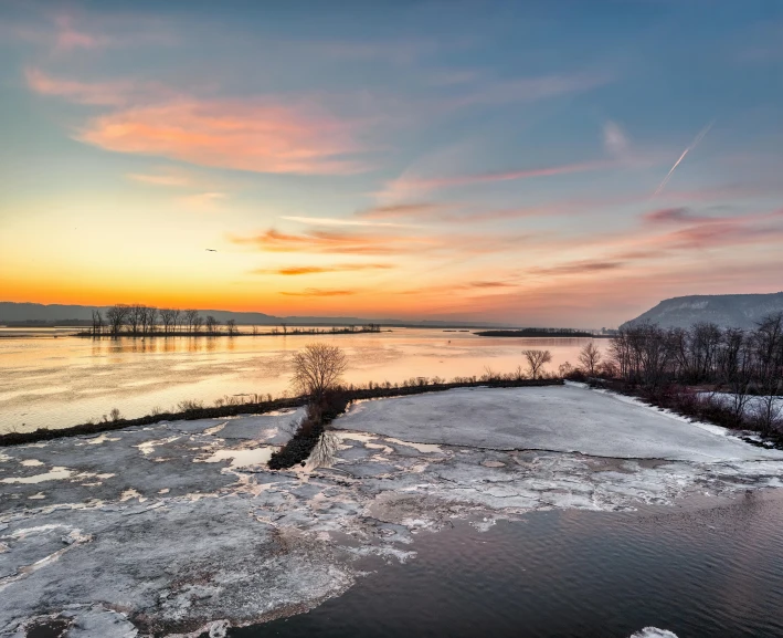 a sunset view with the water frozen and some trees