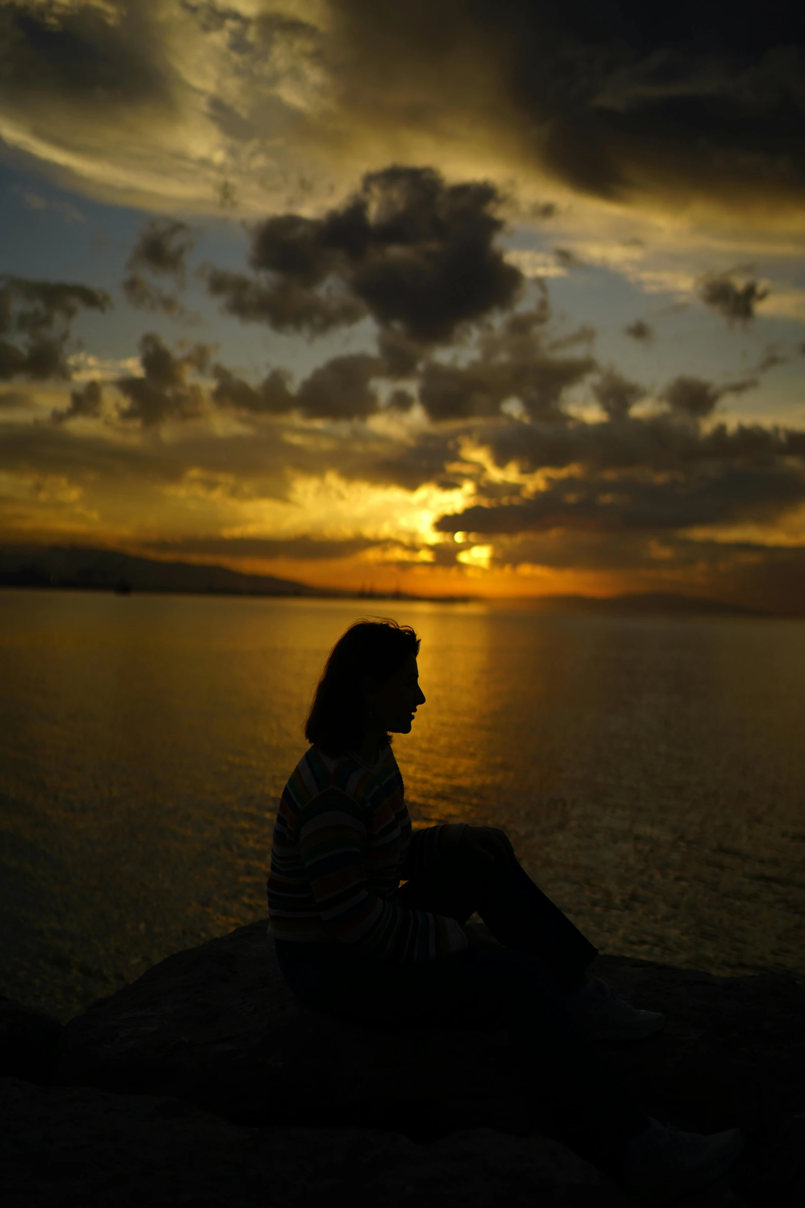 a man sitting on a stone ledge at the waters edge during sunset