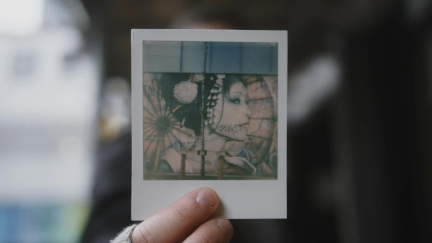 a person holds up a polaroid print of two people